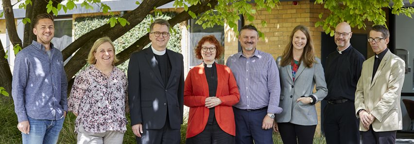 Image depicting three women, and two men who are staff members of Trinity College Theological School and standing in front of the Old Warden's Lodge.